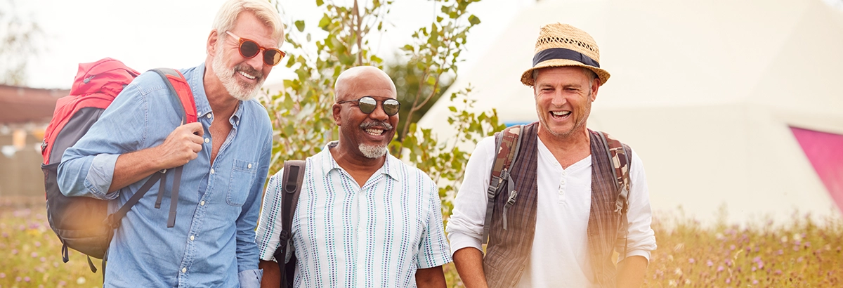 Three men taking a walk while enjoying the outdoors, in a field with flowers, smiling under a bright sky.