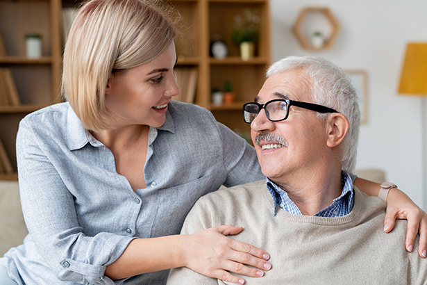 Restful senior man and his daughter relaxing on couch, smiling and looking at each other while talking at home