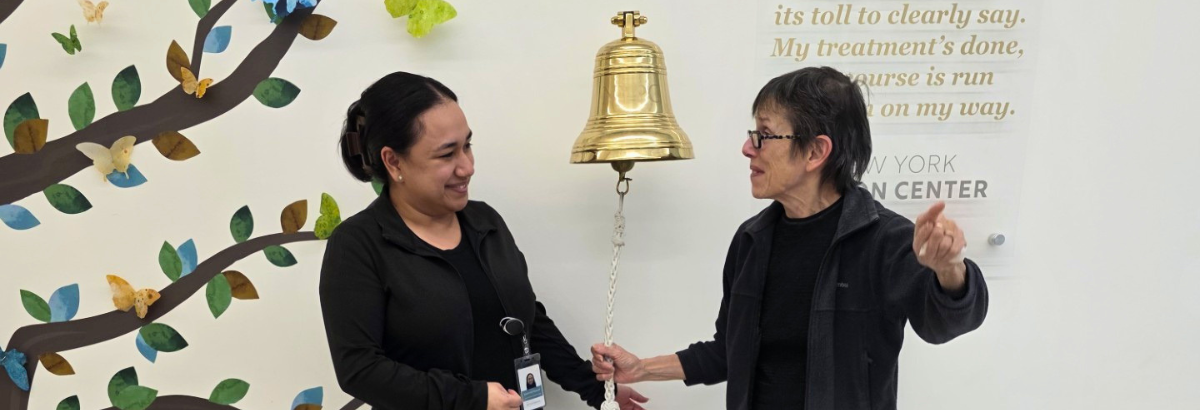 Patient with NYPC staff member posing near the end of treatment bell at NYPC.