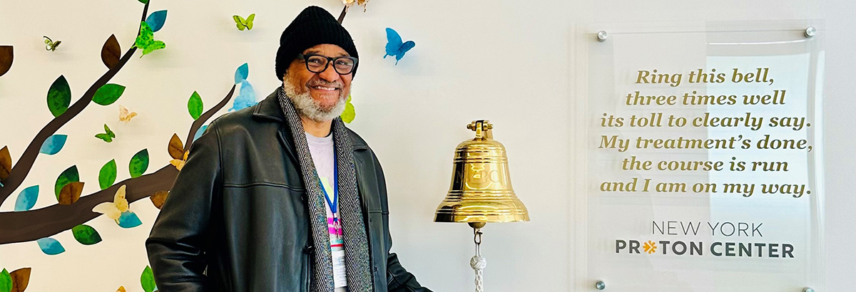 Male patient wearing a black knit hat smiling and ringing last treatment bell