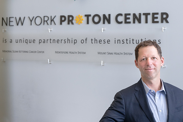 Jonathan Weinbach, CEO of the New York Proton Center stands in front of the center's lobby signage.