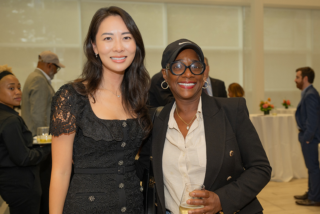 Two women standing side-by-side smiling at a celebratory event with a drink on hand.