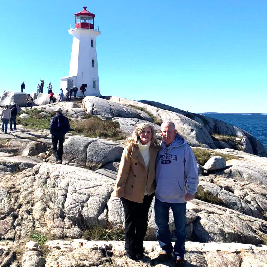 NYPC patient, Debi Walsh Lembo, happily posing with her husband on scenic rocks by the water with a lighthouse in the background.