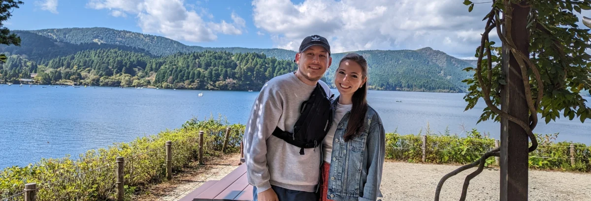 Jack, a former New York Proton Center patient, and his wife smile happily outdoors with mountains and blue skies in the background.