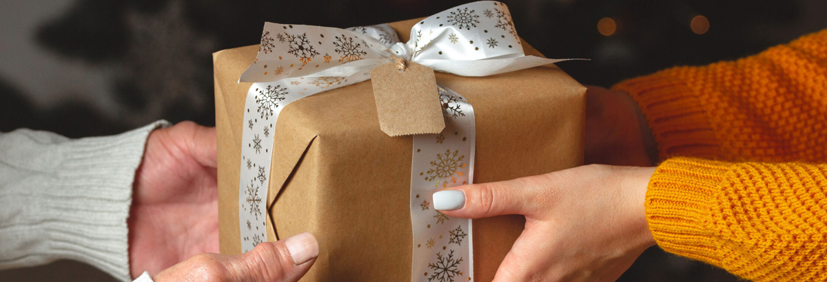 Two sets of hands around a wrapped gift box with ribbon