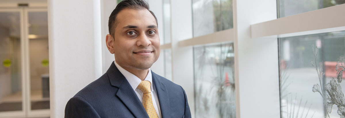 Dr. Shaakir Hasan, physician, standing in front of window at the New York Proton Center.