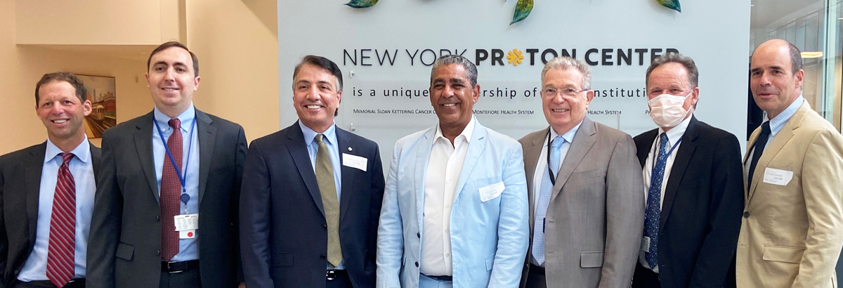 Seven men standing in front of sign in New York Proton Center lobby