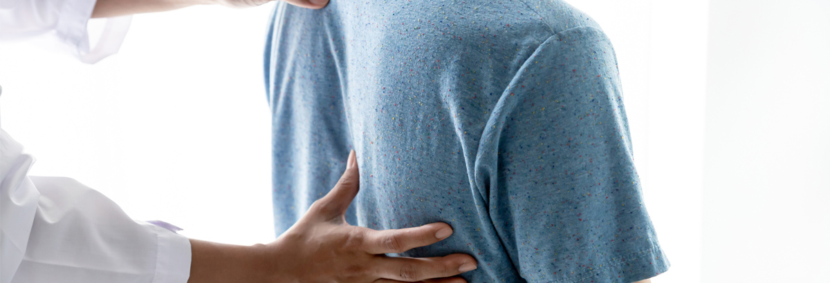 Man in blue t-shirt with back being examined by a doctor