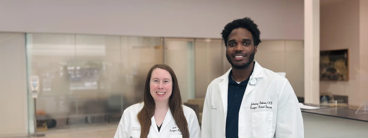 Two members of the New York Proton Center's Dosimetry team, Julie Moreau and Jehvaney Robinson, stand side-by-side in their lab coats with warm smiles.