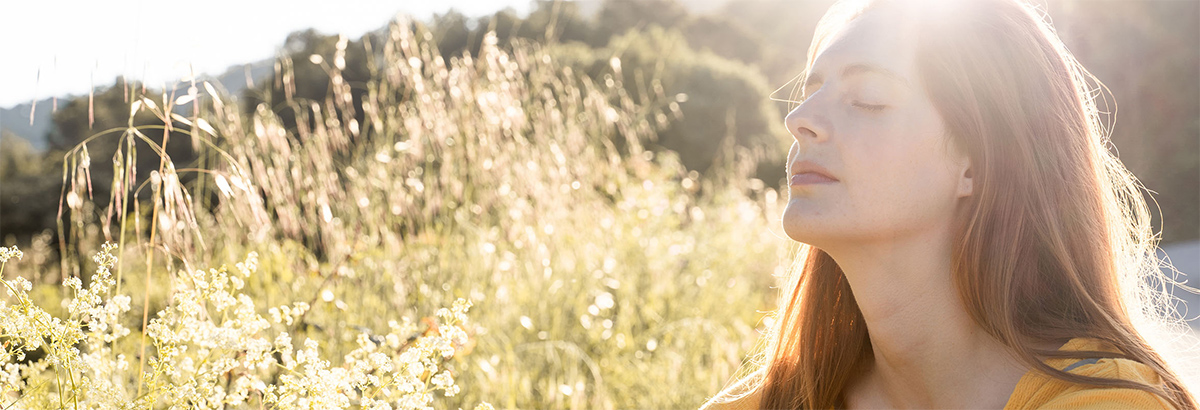 Women sitting in a field on a sunny day with her eyes closed in a contemplative state