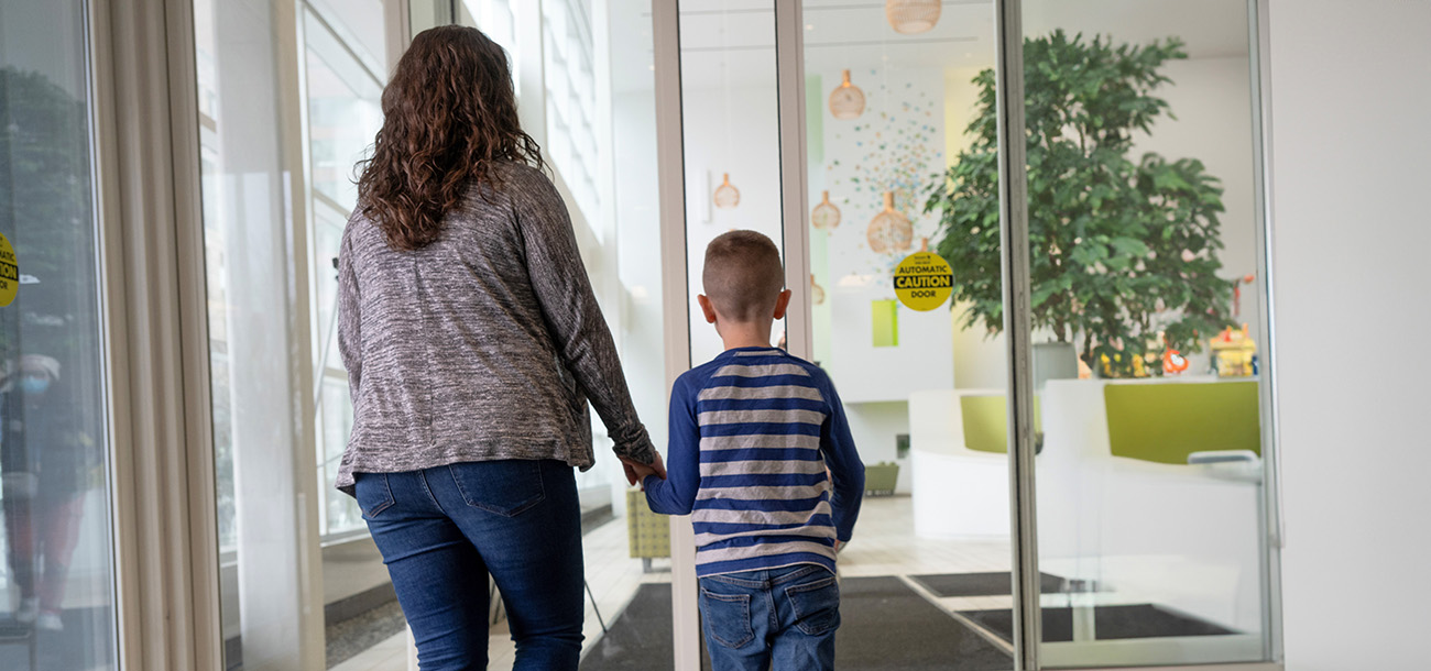 The backs of a mother and her young son walking through the lobby doors of the New York Proton Center.